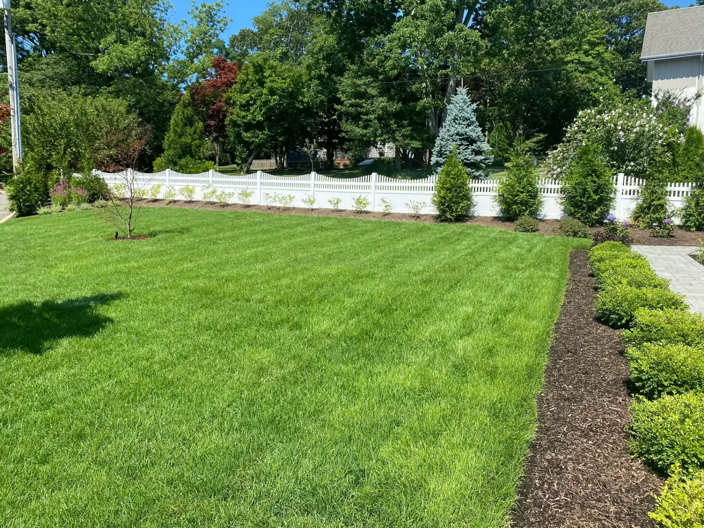 White scalloped vinyl picket fence bordering a manicured lawn and landscaped backyard in NJ