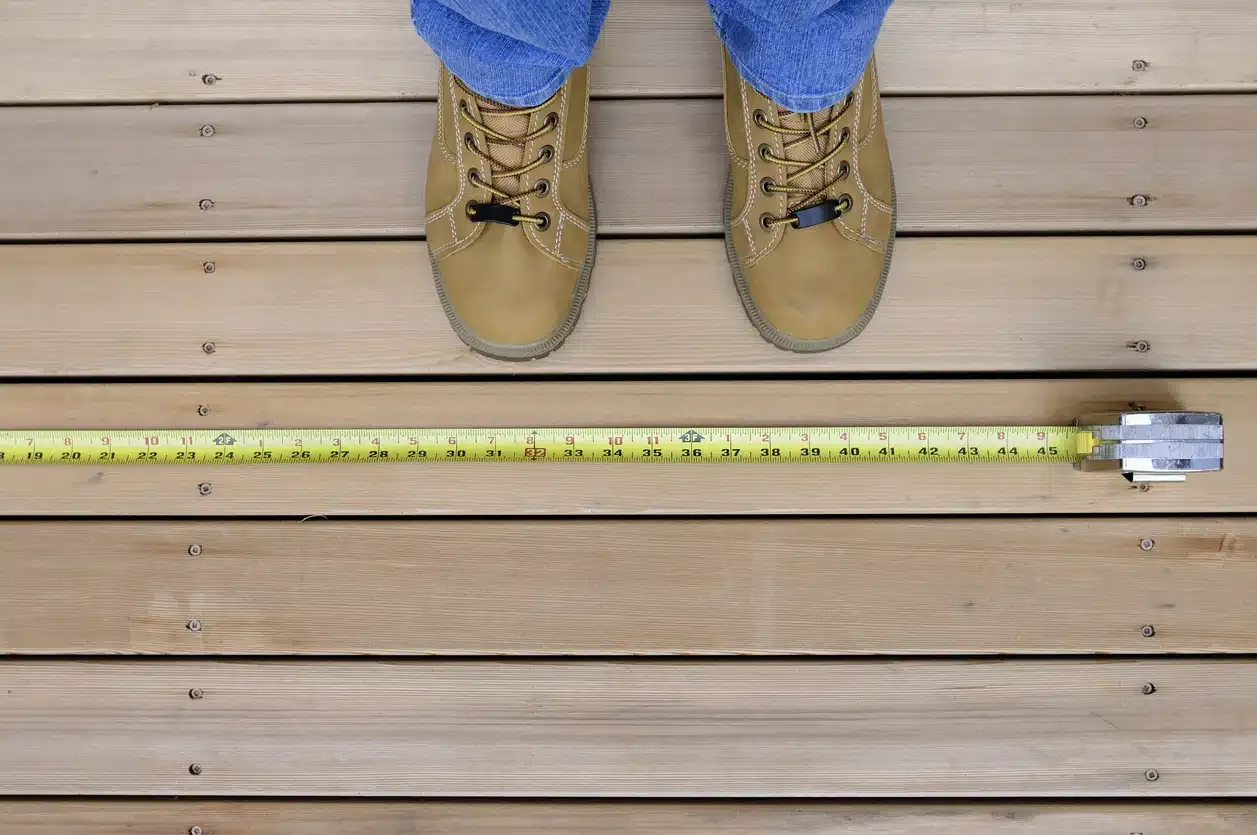 Boots and a tape measure on a wood deck illustrating fence height measurement