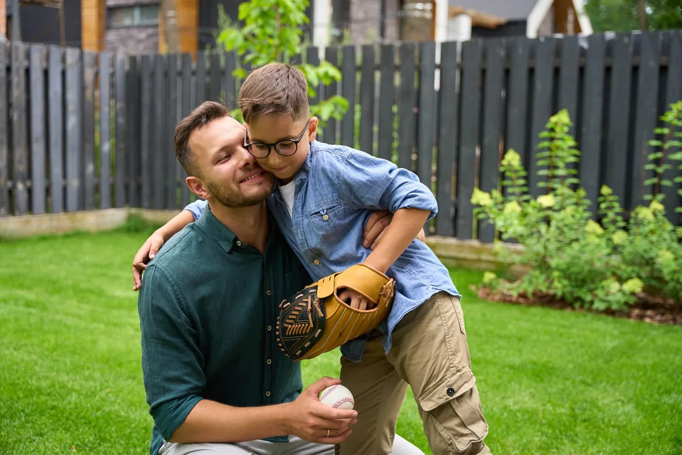 Father and son hugging in a backyard with a wood privacy fence