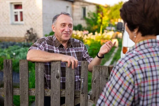 Two neighbors chatting over a wooden picket fence in a New Jersey backyard at sunset
